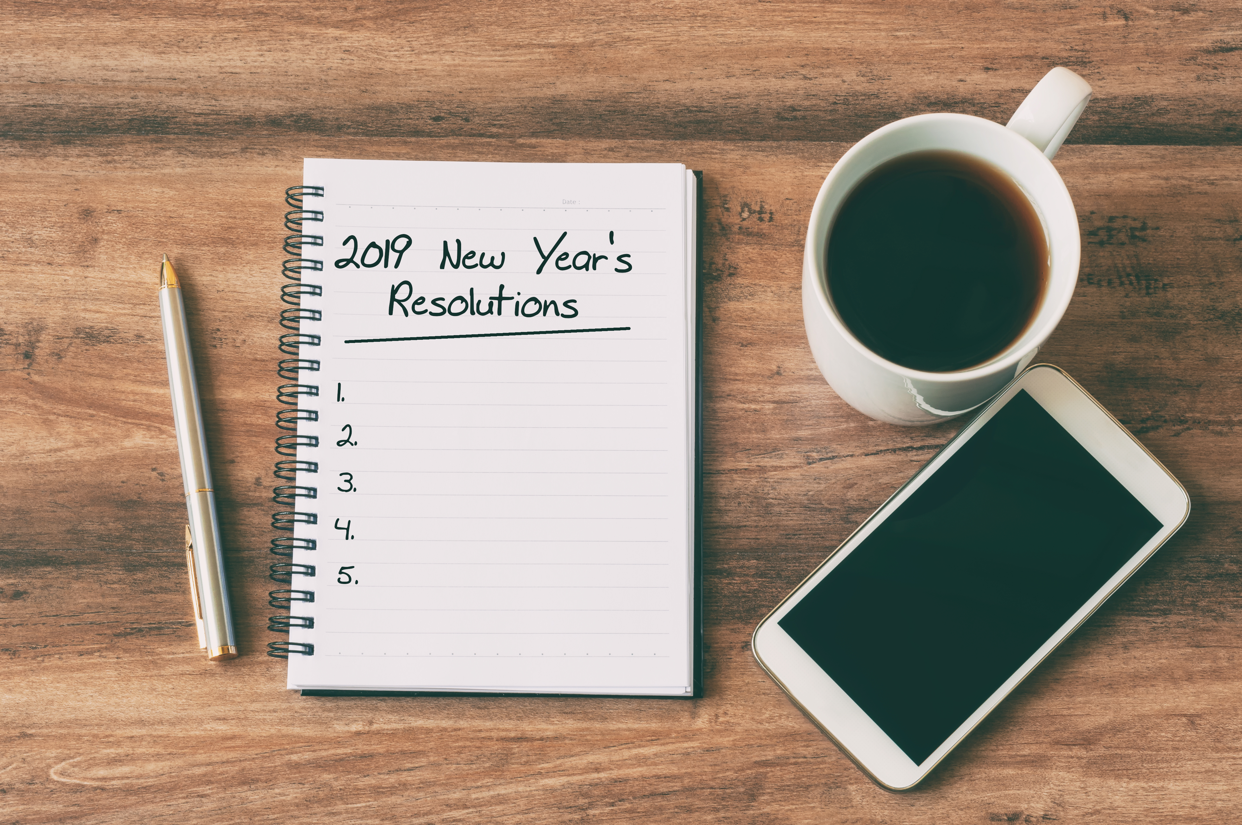 New Year Concept - 2019 New Year's Resolutions Text On Notepad. Smartphone, Pen And Cup Of Copy Background.